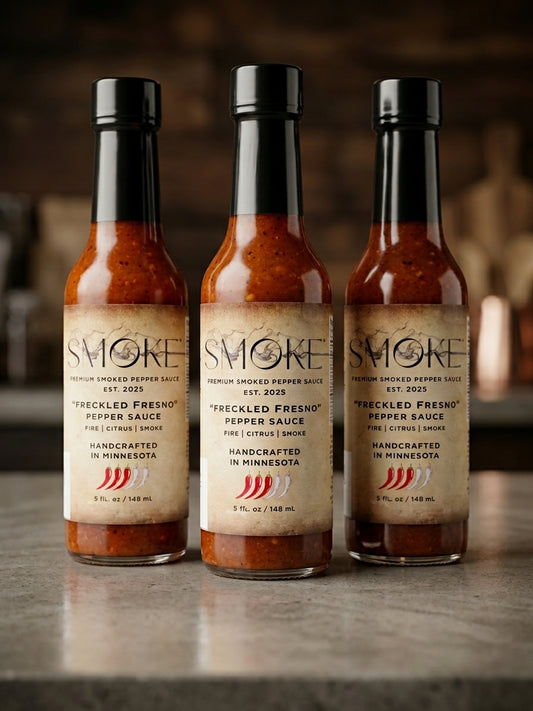 Three clear glass bottles of Smoke Premium Smoked Pepper Sauce Freckled Fresno flavor standing upright on a countertop