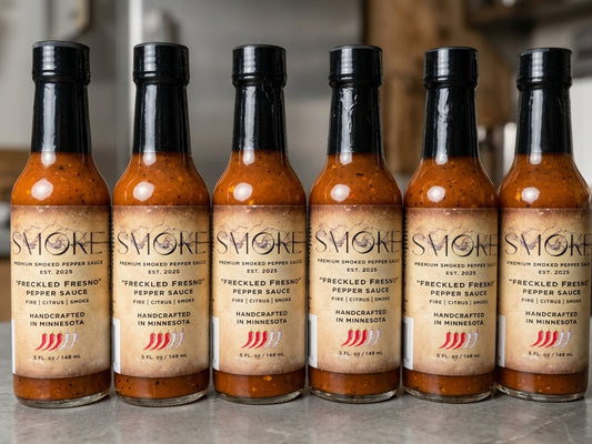 Six clear glass bottles of Smoke Premium Smoked Pepper Sauce Freckled Fresno flavor arranged in a straight row standing upright